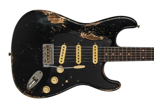 Close-up of a black electric guitar body with a worn finish, gold pickups, and a tremolo bridge.